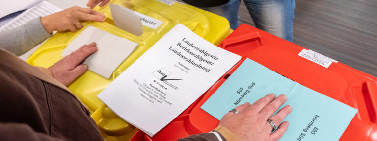 Wahllokale in Nürnberg: Auf den Deckeln der Wahlurnen, hier große rot und gelbe Tonnen, sieht ruhen die Hände der Wahhlhelfer. Farbige Wahlzettel zeigen, in welche Tonne, welcher Stimmzettel eingeworfen werden muss.